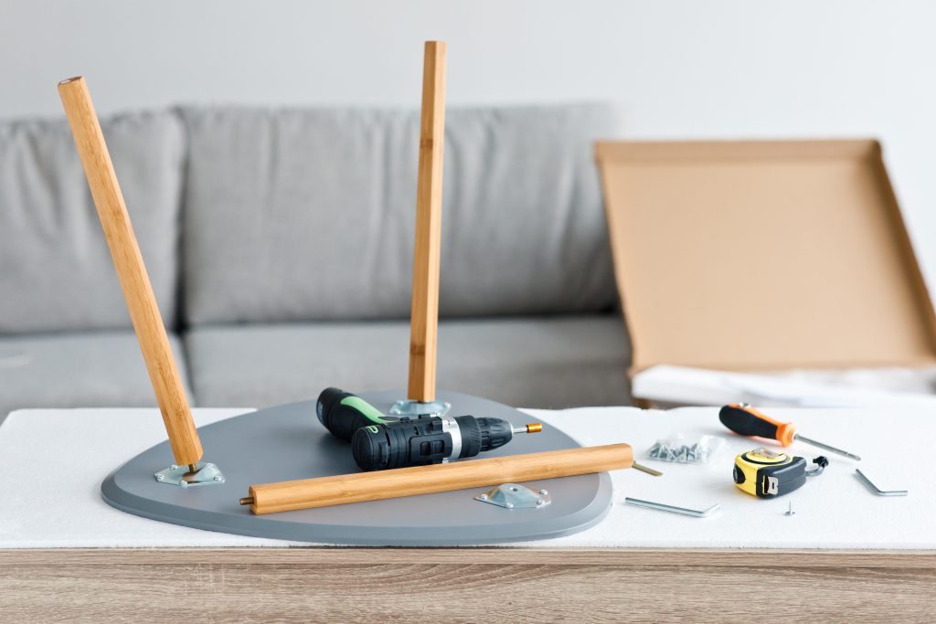 Drill, tool and another equipment on wood table, assembly furniture, improvement or repairing home interior and ideas. Electric screwdriver, chair and parts in living room with boxes, copy space