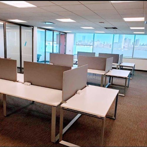 A vacant office space featuring desks arranged neatly and a large window allowing natural light to enter.