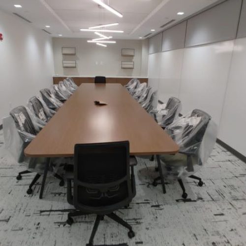 A large, modern conference room featuring a long wooden table with task chairs, minimalist design, and ample lighting.