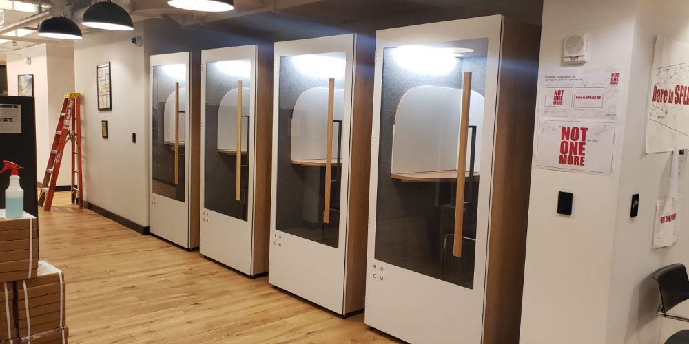 A row of sleek soundproof booths in a modern office setting, featuring wooden accents and glass doors.
