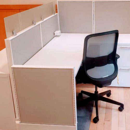 A modern office cubicle featuring a sleek white desk, a black ergonomic chair, and grey partitions for privacy.