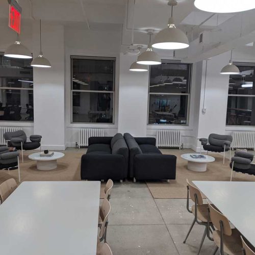 A modern lounge area featuring gray sofas, armchairs, and a circular table, illuminated by pendant lights.